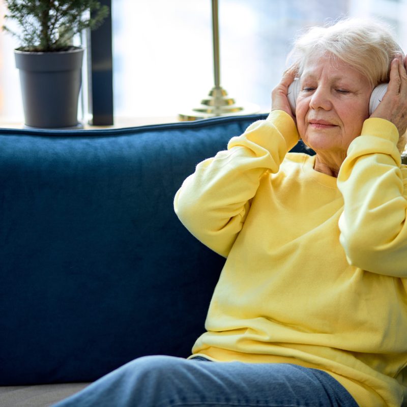 Old people, emotion and technology concept: elderly caucasian woman listen to music with headset, enjoy having rest alone, at weekends. pretty lady with grey hair in casual clothes